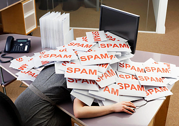 mujer derrumbada sobre una mesa de ordenador y curbierta de folios con spam impreso en rojo